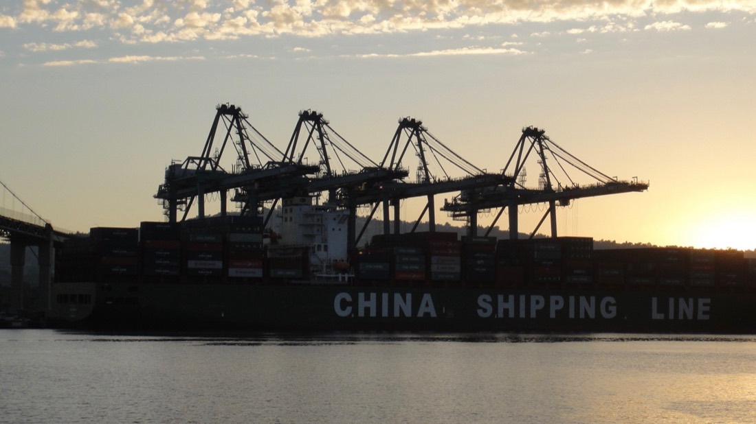 A China Shipping Line container vessel at berth beneath four ship-to-shore cranes at sunset